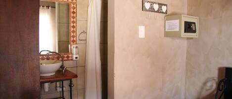 A bathroom with a sink, mirror, and shower curtain. There is a small cabinet with a paper note on the wall.