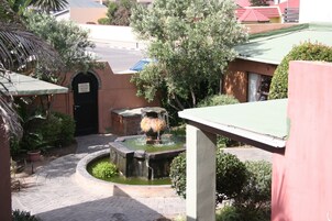 Un patio con una fuente, plantas en macetas y un sendero de ladrillo.
