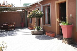 Un patio con suelo de ladrillo, una mesa y sillas de madera, y plantas en macetas.