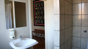 Un baño con un lavamanos blanco, un espejo, cortina de ducha y zona de ducha con azulejos.