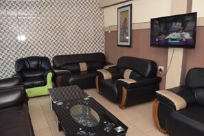 A living room with a checkered floor, a flat-screen TV mounted on the wall, and a framed picture above it. - De'elites Pool Bar & Inn (Port Harcourt)