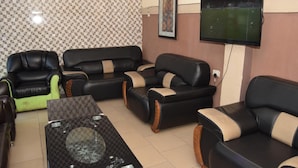 Ein Wohnzimmer mit schwarzen Ledersofas, einem Glastisch und einem an der Wand befestigten Fernseher.