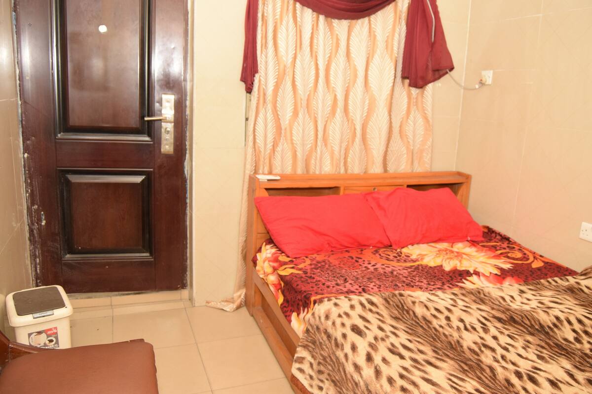 A bedroom with a wooden bed, red pillows, a leopard print blanket, a wooden nightstand, and a door with a handle.