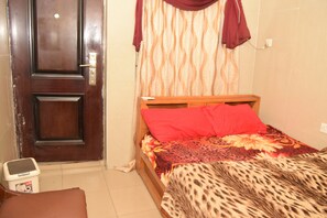 A bedroom with a wooden bed, red pillows, a leopard print blanket, a wooden nightstand, and a door with a handle. - De'elites Pool Bar & Inn (Port Harcourt)