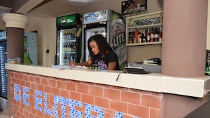 Eine Bar mit einer gefliesten Theke, einem mit Getränken gefüllten Kühlschrank und Regalen voller Flaschen.