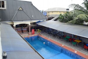 A swimming pool with a covered patio area, outdoor seating, and a view of the surrounding buildings. - De'elites Pool Bar & Inn (Port Harcourt)