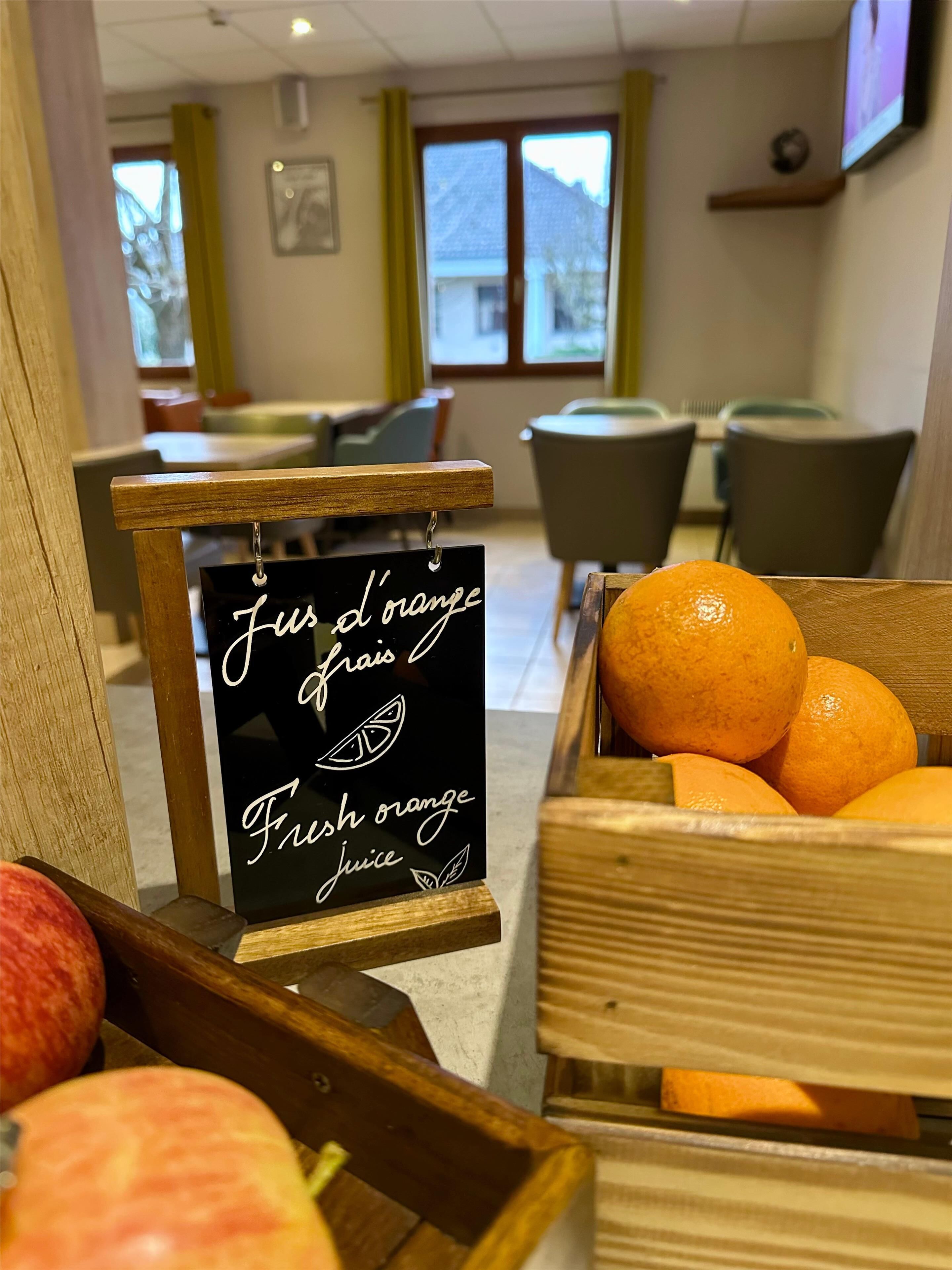 Desayuno con un cartel que indica jugo de naranja recién exprimido, una caja de madera con naranjas y una mesa de madera.