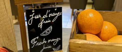 Desayuno con un cartel que indica jugo de naranja recién exprimido, una caja de madera con naranjas y una mesa de madera.