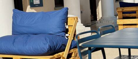 Entrada de hotel con un cartel que dice 'Welcome', asientos exteriores con cojines azules y muebles de madera.