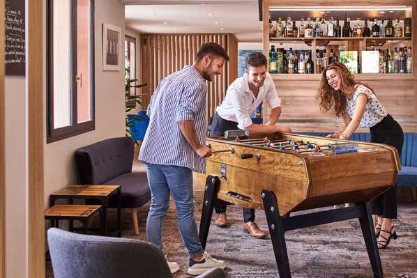 A bar area with a foosball table, seating, and a bar stocked with bottles. - Kyriad Sens (Malay-le-Grand)
