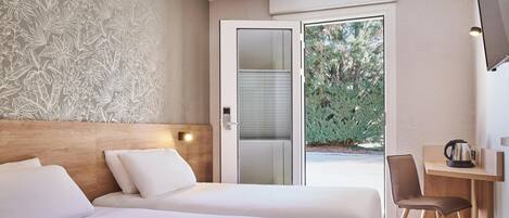 A hotel room with two beds, a desk, a chair, a TV, and a sliding glass door leading to a garden.