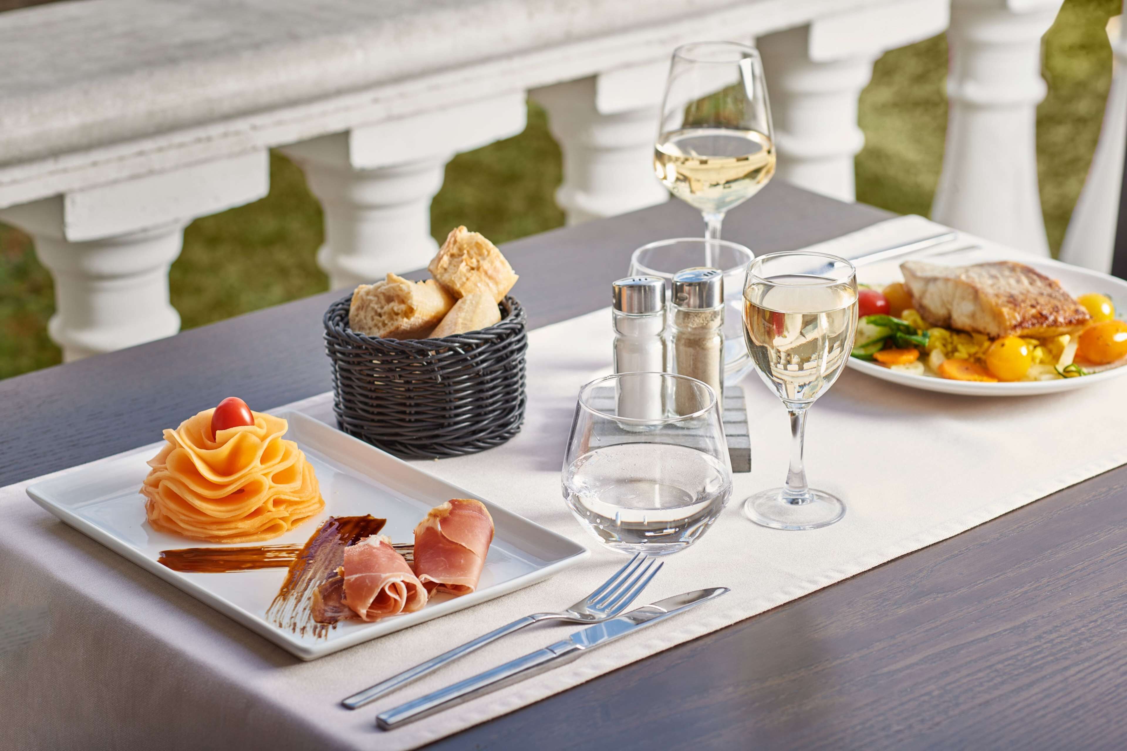 A dining table with a white tablecloth, a basket of bread, a plate of food, a glass of white wine, and salt and pepper shakers.