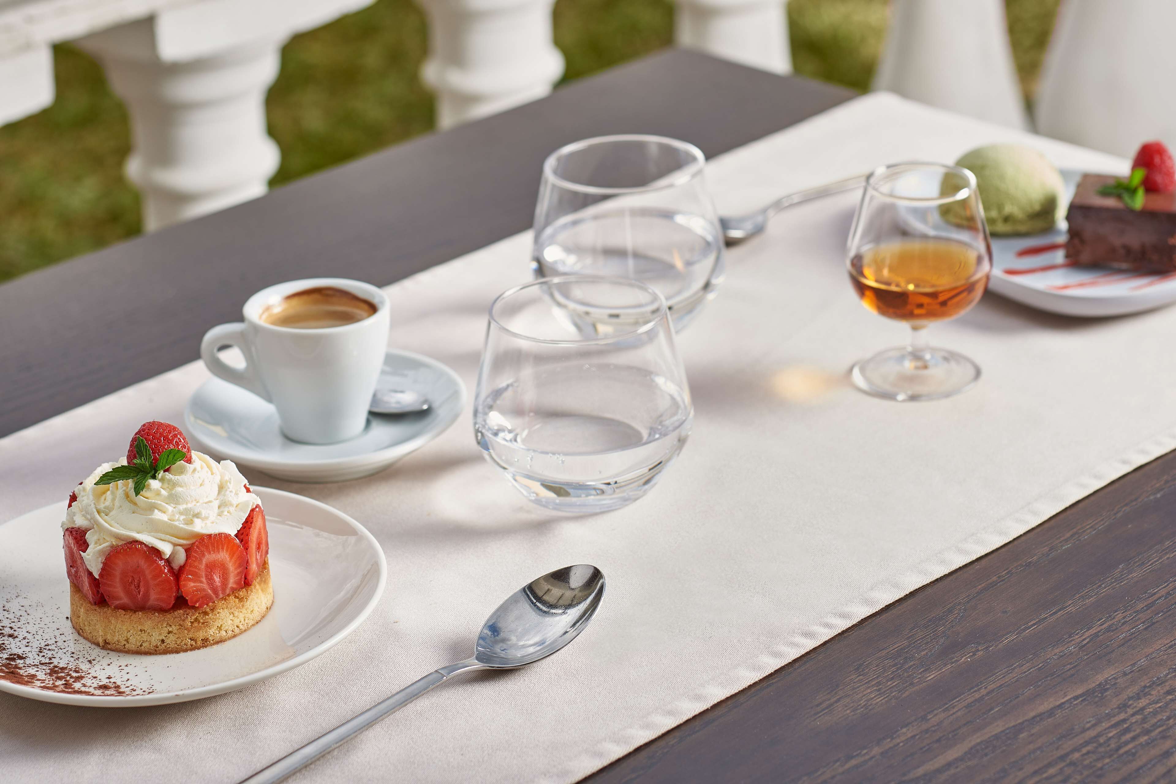 A table with a dessert, a cup of coffee, and a glass of wine, set on a tablecloth.