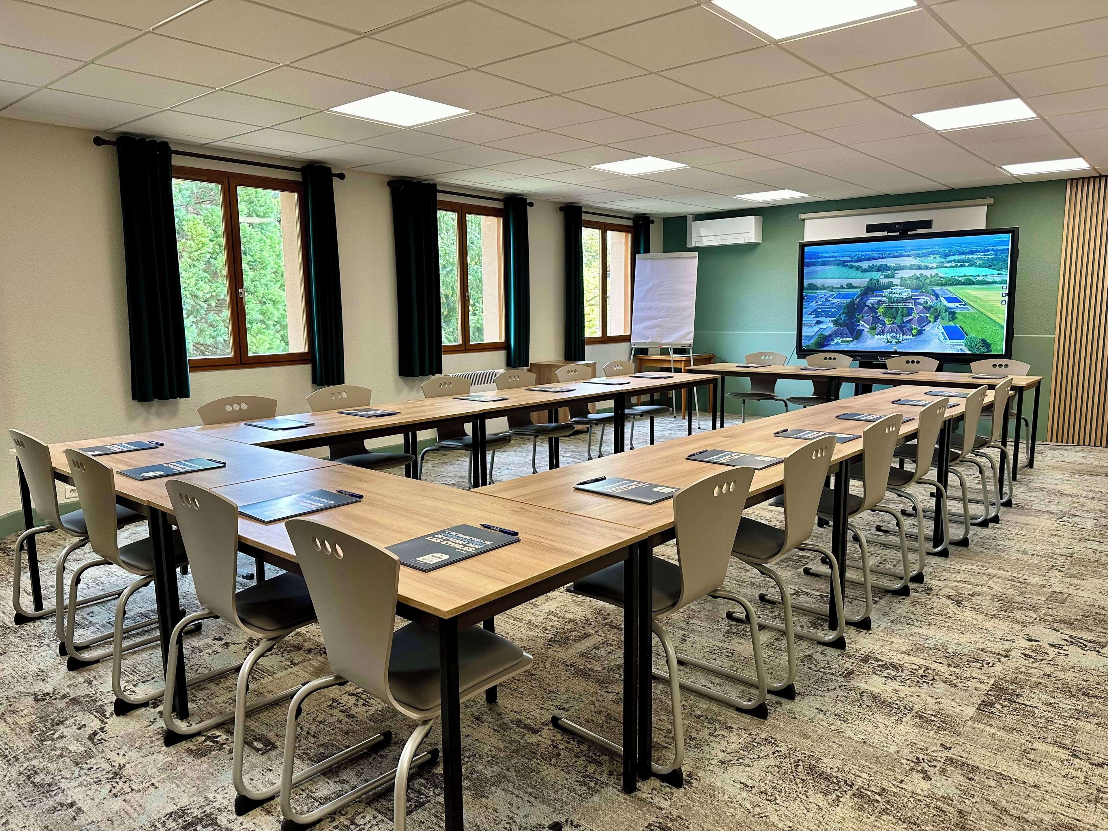 Una sala de conferències amb taules llargues, cadires, una pantalla de projector i una pissarra.