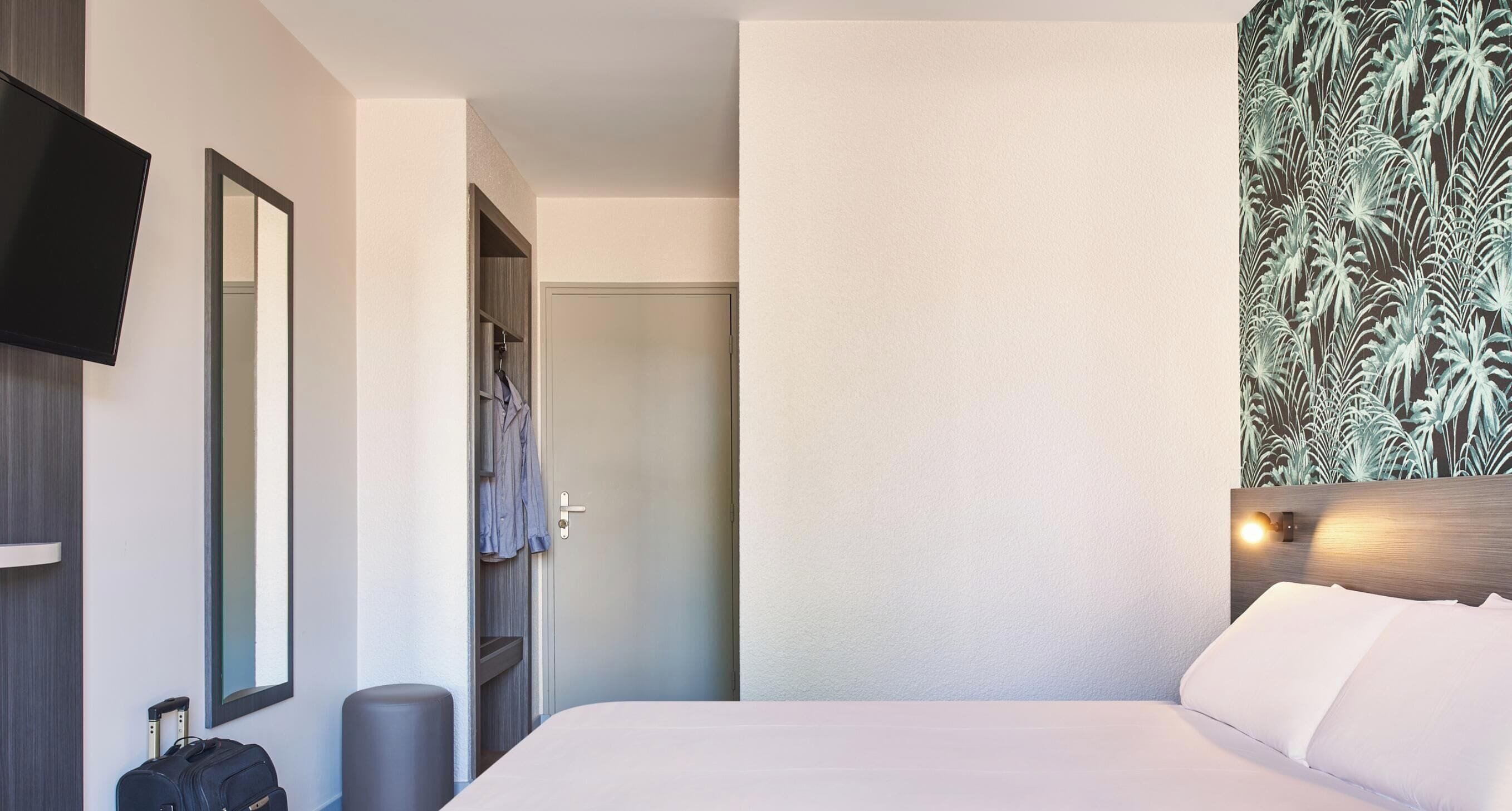 Ein Hotelzimmer mit Bett, Fernseher, Kleiderschrank und Badezimmertür.