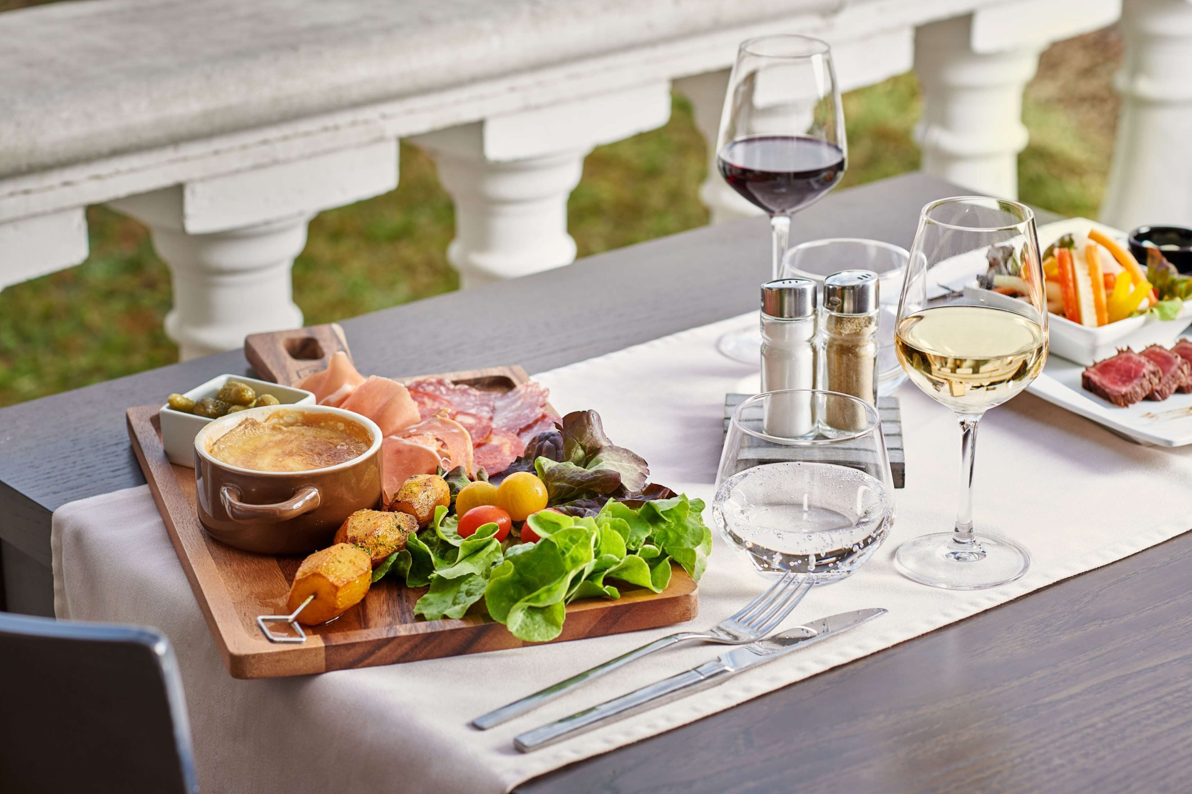 A table set with a charcuterie board, a bottle of wine, and a glass of white wine on a terrace.