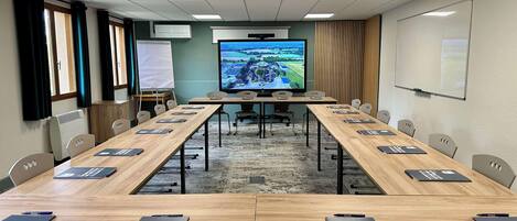 A conference room with a long table, chairs, a large screen, and a whiteboard.