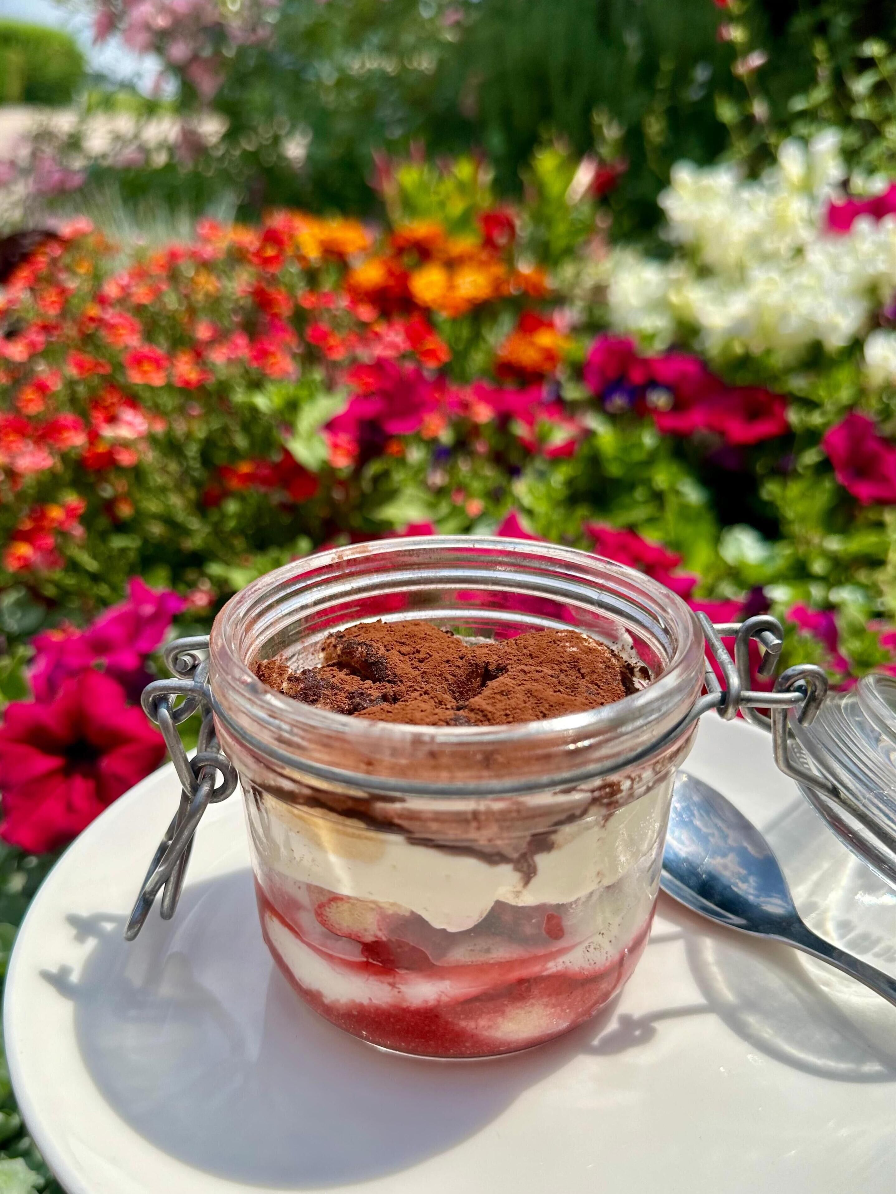 Un postre en un frasco de vidrio con cierre metálico, sobre un plato blanco con una cuchara al lado.