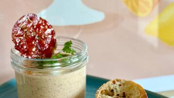 A glass jar of creamy spread with a dried fruit garnish on a blue plate, accompanied by a slice of bread.