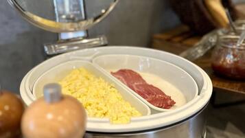 A kitchen counter with a food warming tray containing scrambled eggs and sliced meat.