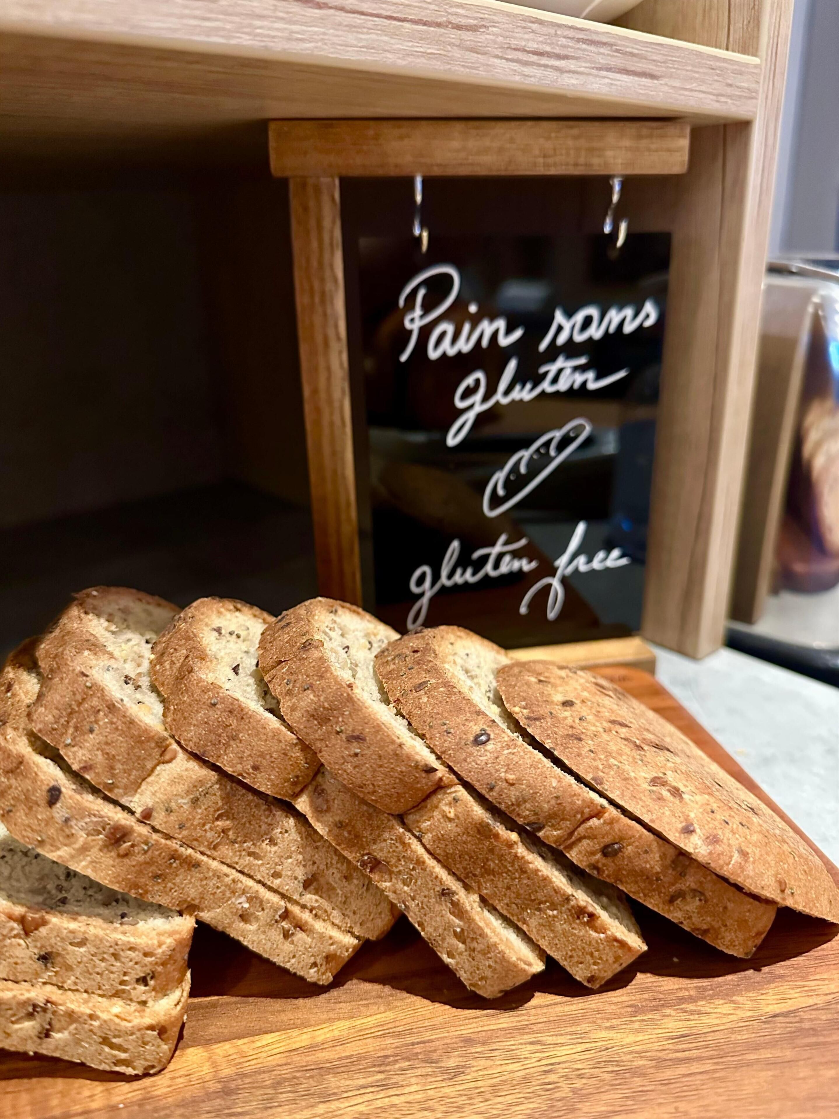 Slices of gluten-free bread on a wooden board with a sign stating "Pain dans gluten free."