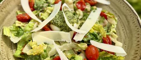 A plate of mixed greens salad with tomatoes, onions, and cheese, served on a ceramic plate.