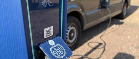 Estación de carga con un código QR y un cable conectado a un vehículo.
