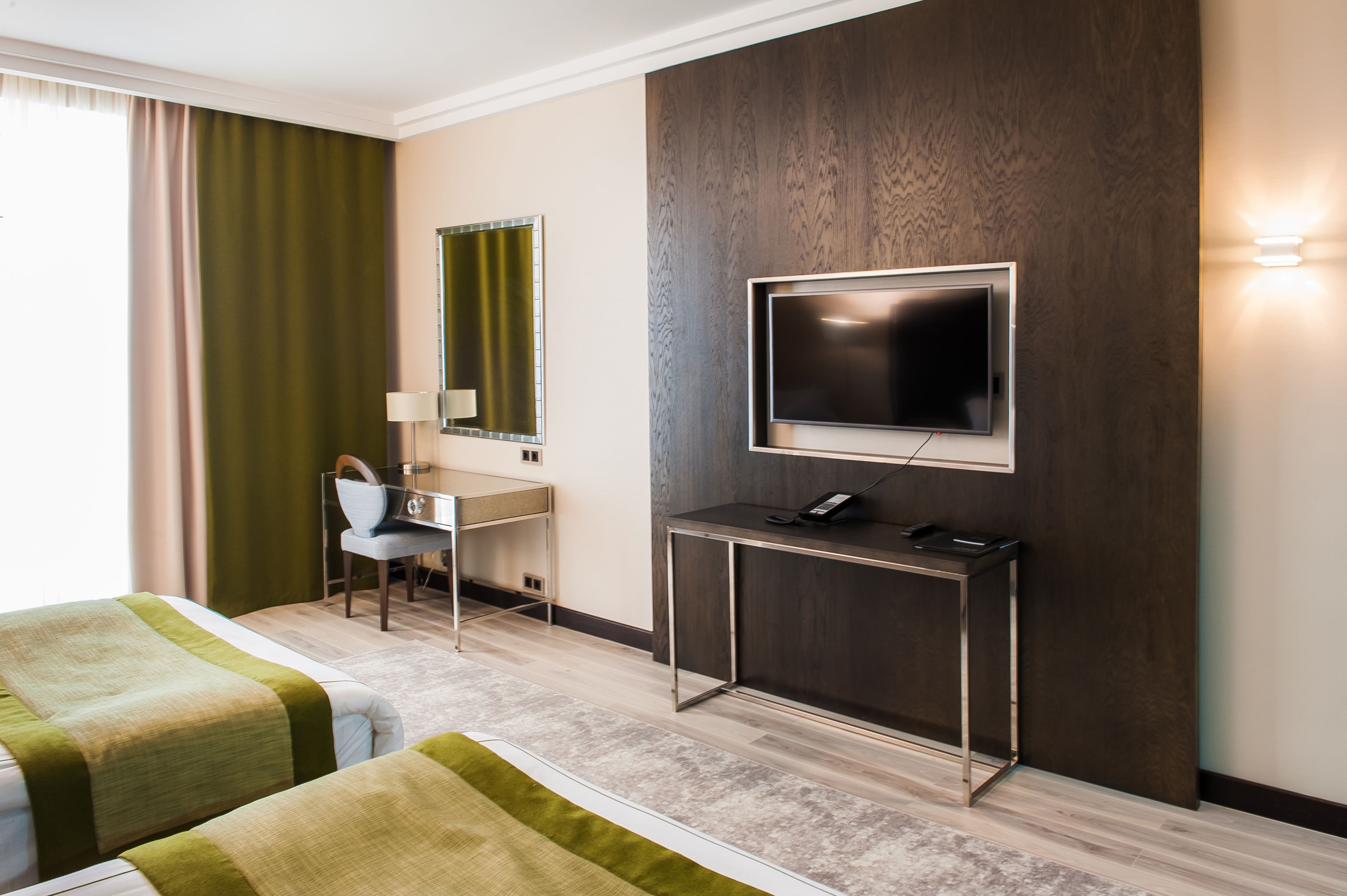 Habitación de hotel con dos camas, un escritorio con silla, un televisor montado en la pared y una mesita con teléfono.