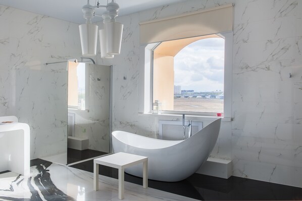 Un baño moderno con una bañera independiente, una mesita pequeña y un ventanal con vistas a la ciudad.