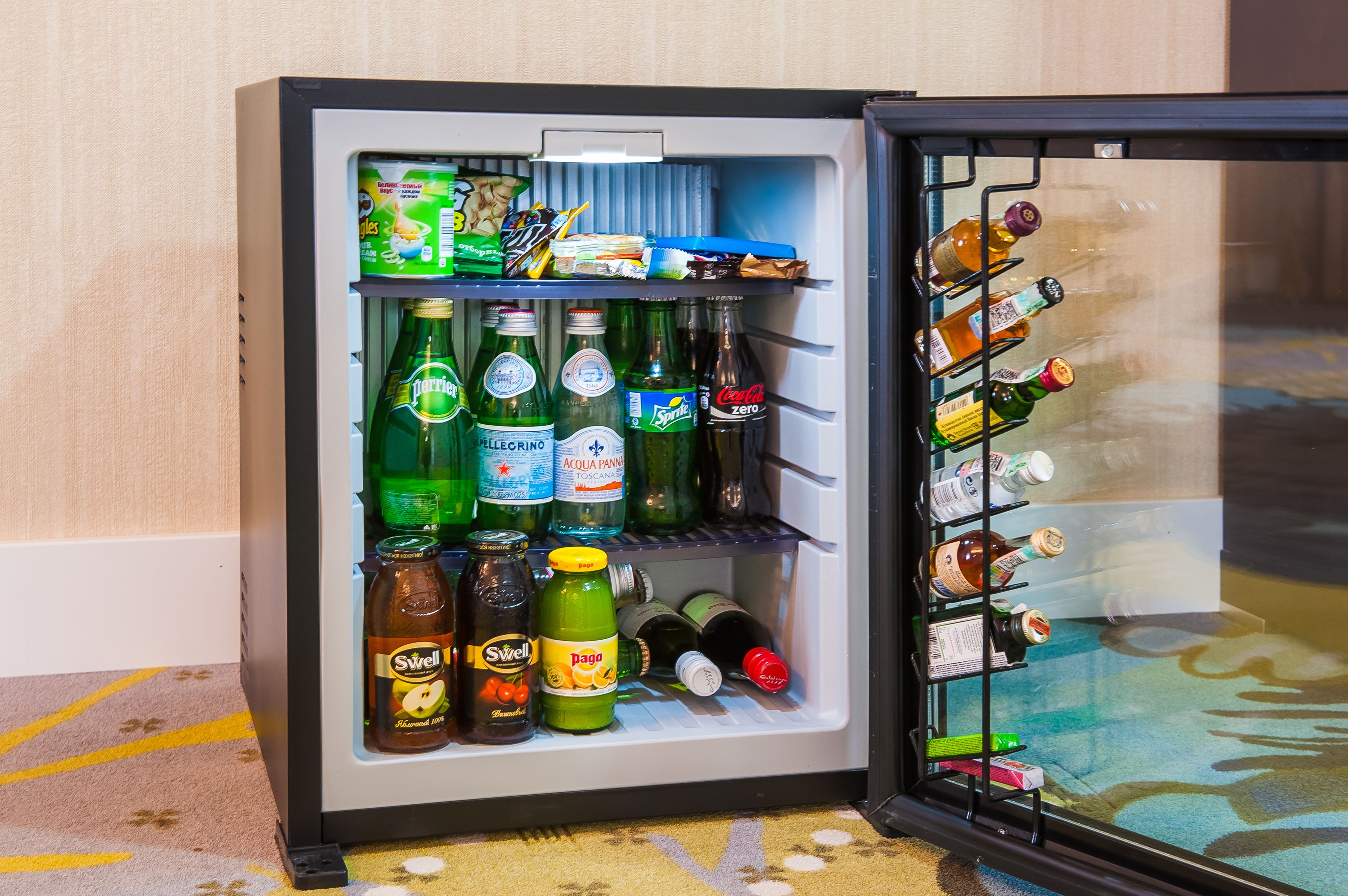 Un mini refrigerador con una variedad de bebidas, incluyendo cerveza, refrescos y jugo.