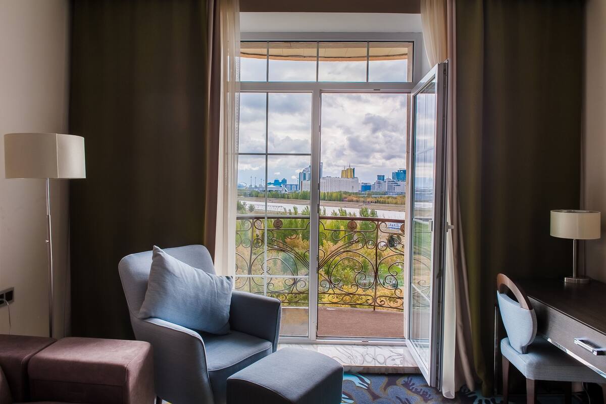 Une chambre d’hôtel avec un balcon, un bureau, une chaise et une lampe.