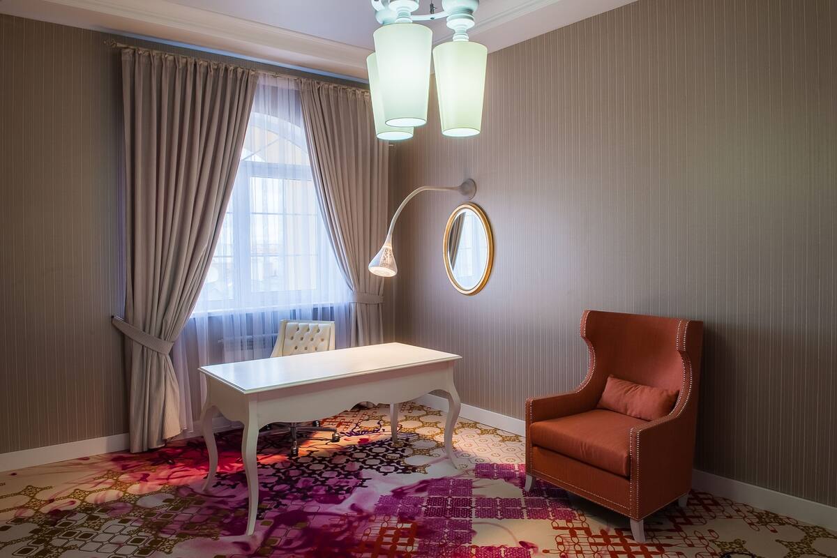 Une pièce avec un bureau blanc, un fauteuil rouge, un miroir et un tapis à motifs.