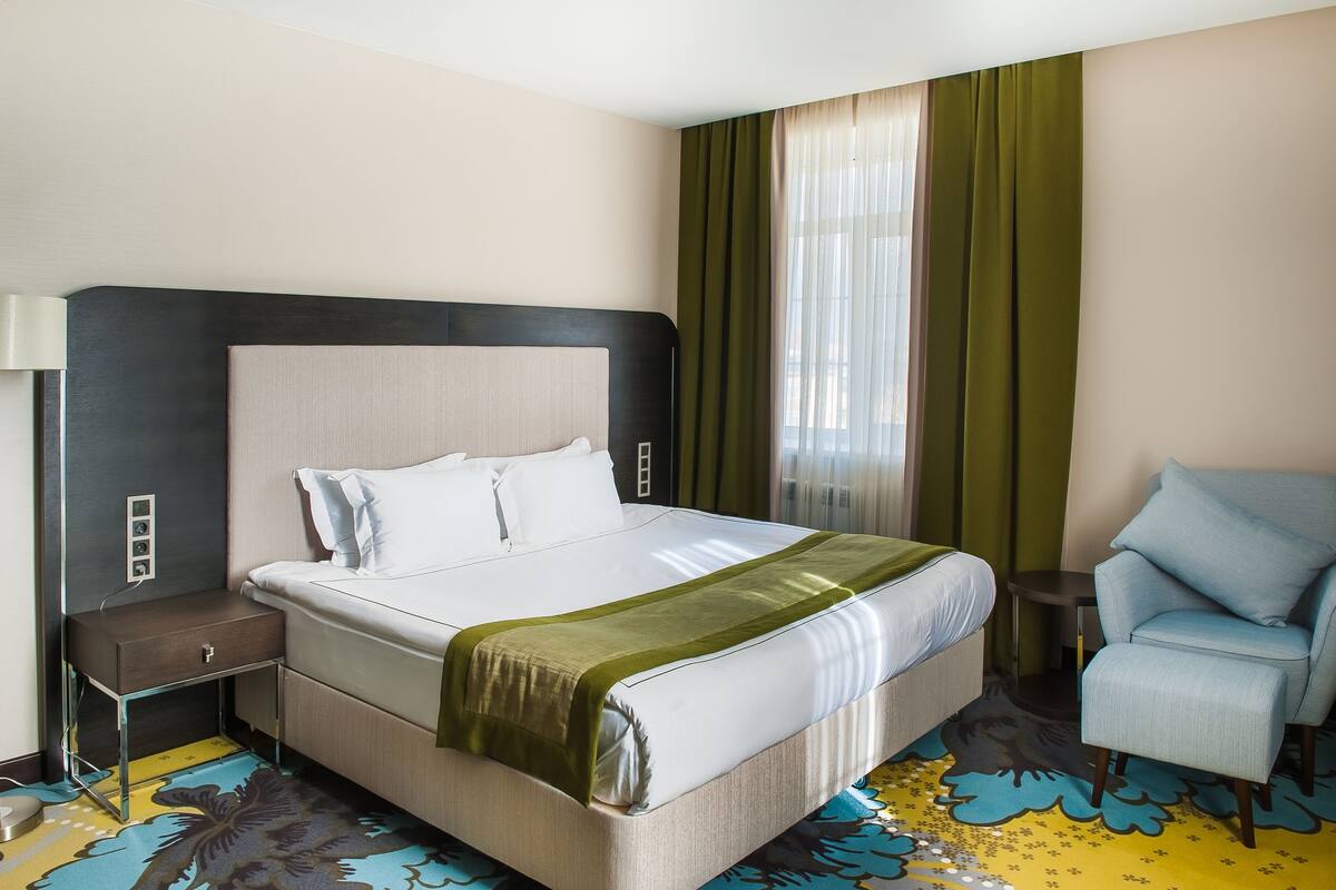 Une chambre d’hôtel avec un grand lit, une table de chevet, une chaise et une fenêtre avec des rideaux.