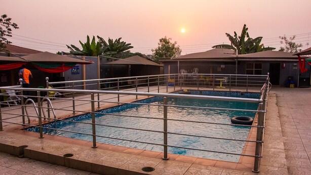 A swimming pool with a metal safety railing, surrounded by a tiled walkway. - Duckland Hotel and Suites Ltd (Ikorodu)