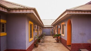 A corridor with a series of rooms, each with a window and a door, and potted plants along the walkway. - Duckland Hotel and Suites Ltd (Ikorodu)