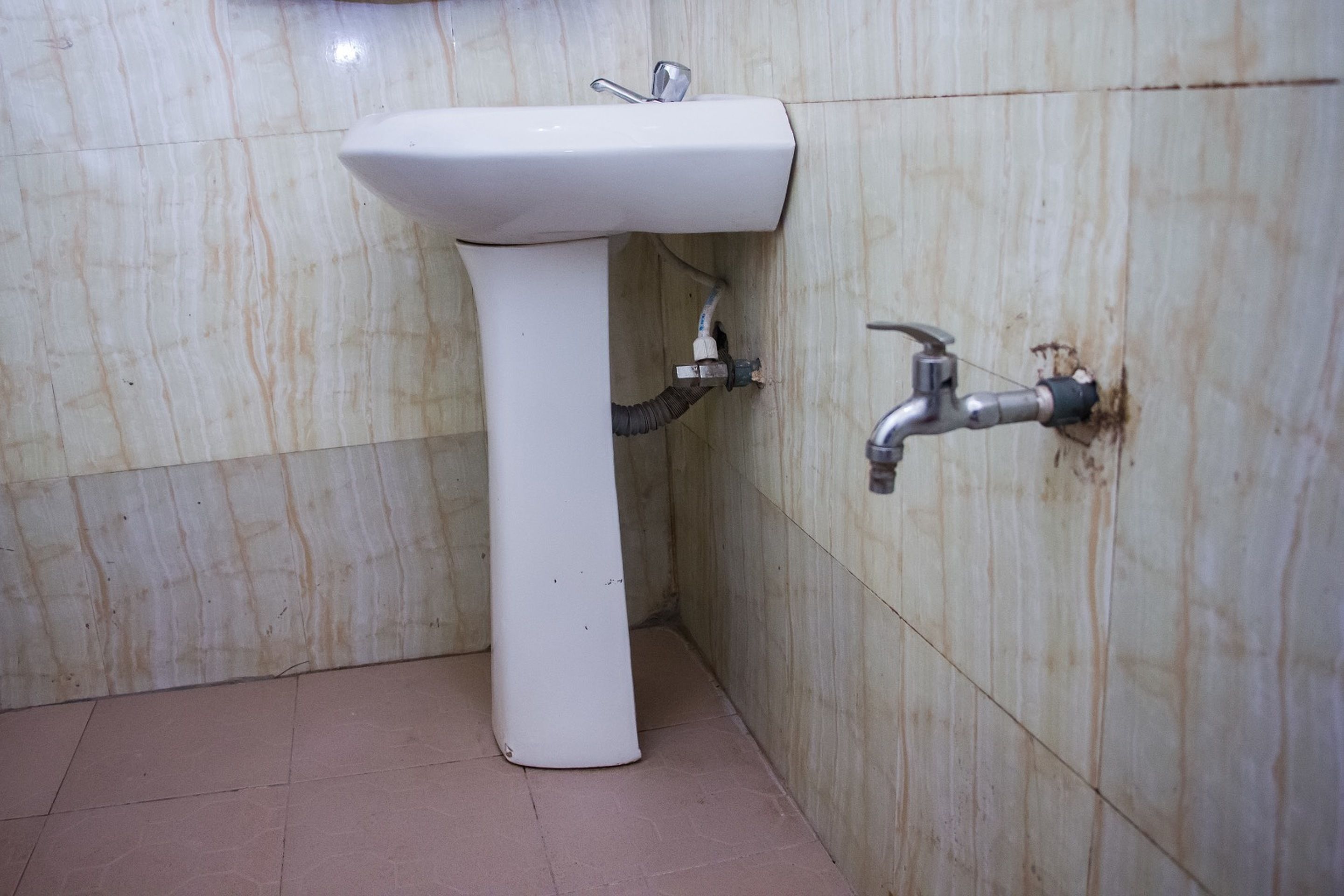 A bathroom with a white pedestal sink, a wall-mounted faucet, and tiled walls.