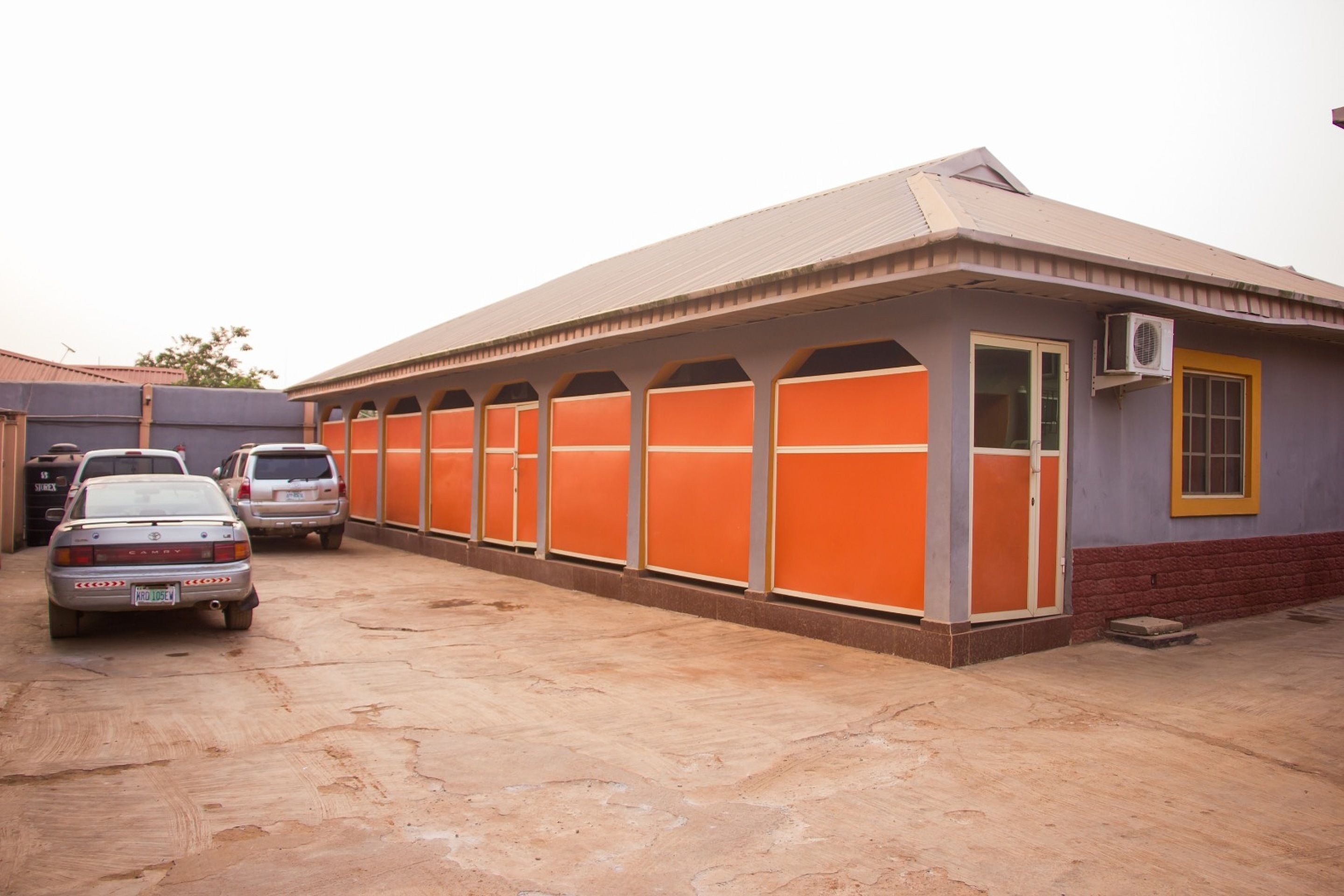 A building with a covered parking area, multiple vehicles, and a red and yellow exterior.