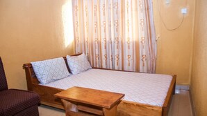 A single bed with a wooden frame and a matching wooden table in front. - D Jos Hotel (Ijede)