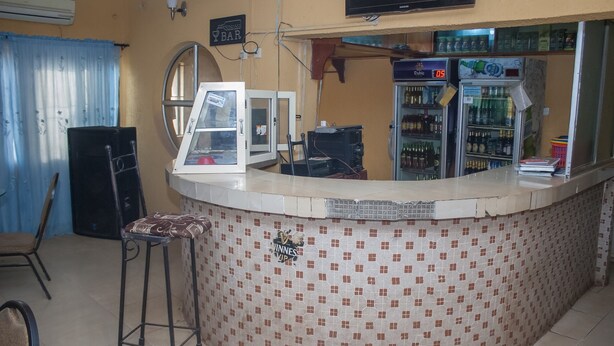 A bar area with a tiled counter, a television mounted on the wall, and a refrigerator stocked with beverages. - D Jos Hotel (Ijede)