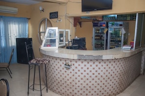 A bar area with a tiled counter, a television mounted on the wall, and a refrigerator stocked with beverages. - D Jos Hotel (Ijede)