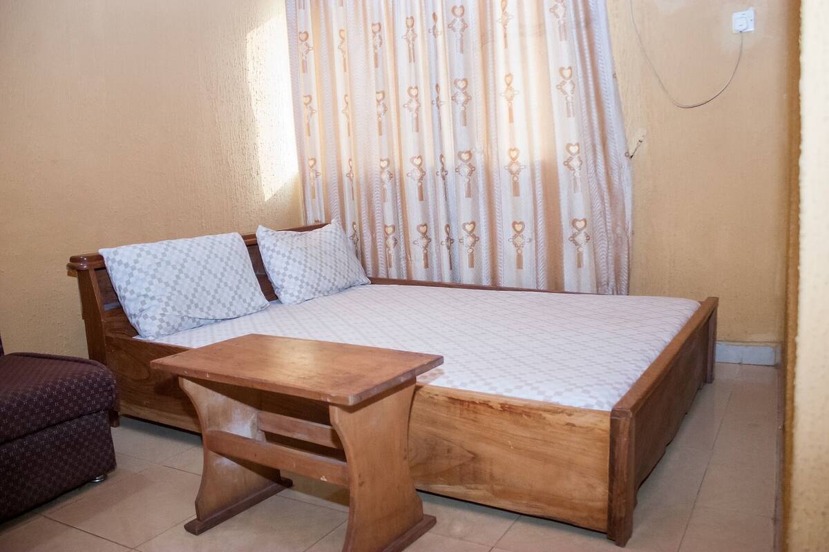 Un dormitorio con una cama de madera, una mesita de madera, un cojín estampado y una cortina con diseño de llave.
