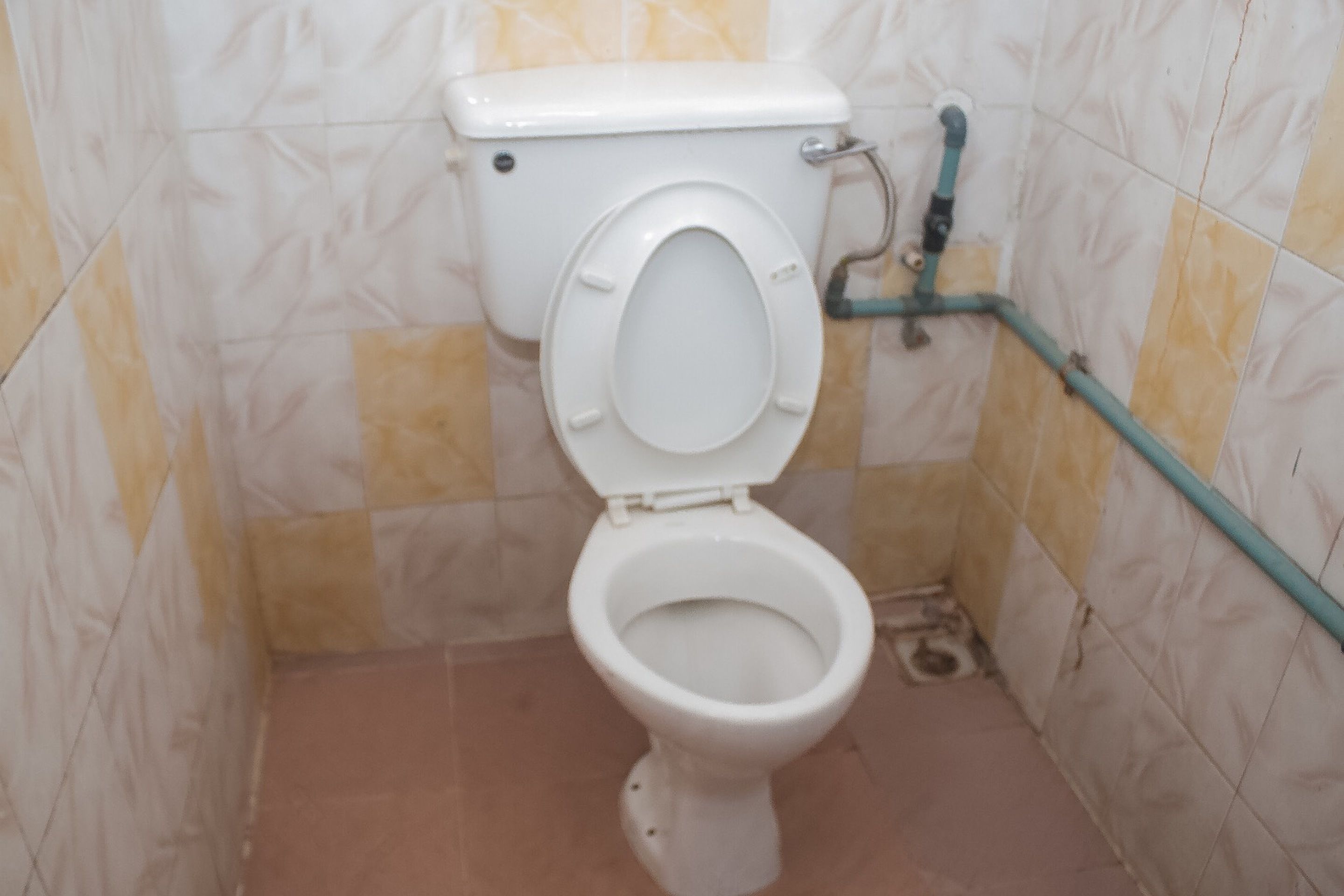 Inodoro con asiento elevado, palanca de descarga y una tubería a lo largo de la pared.
