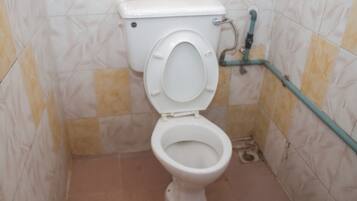 Inodoro con asiento elevado, palanca de descarga y una tubería a lo largo de la pared.