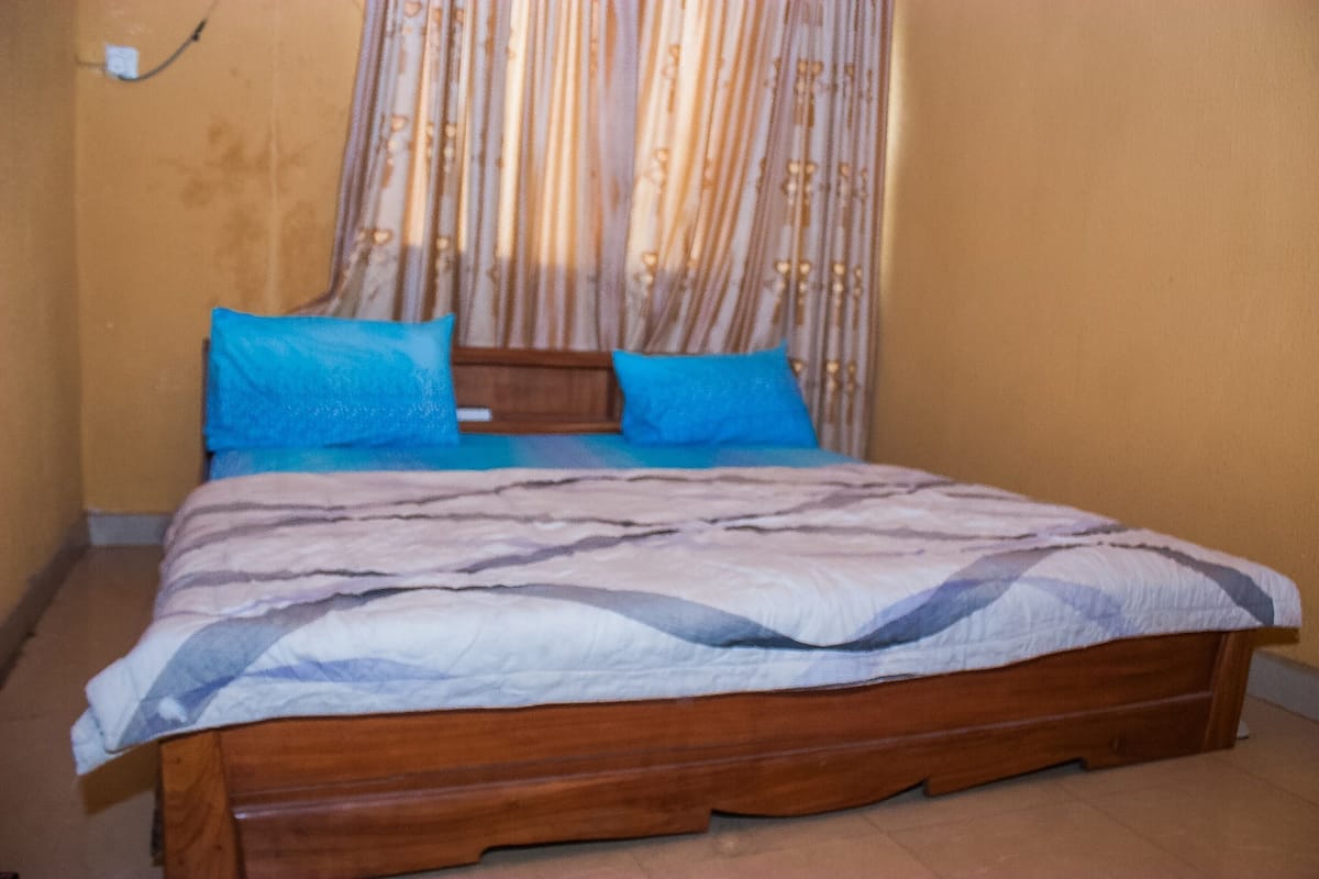 Una cama de madera con una colcha estampada y dos almohadas, una cortina con diseño floral y un enchufe de pared.