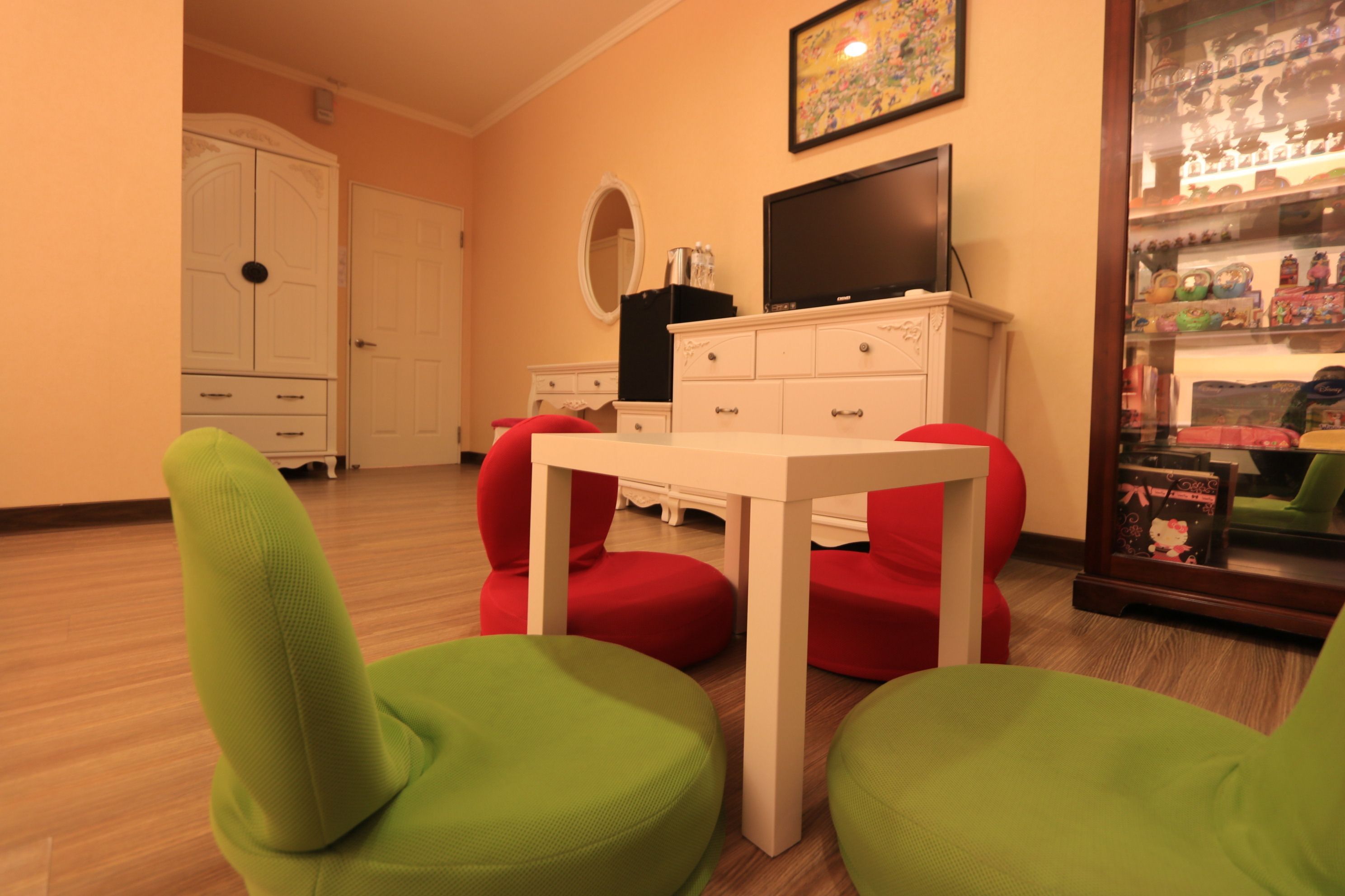A room with a white table and green chairs, a television, and a display cabinet with figurines.