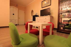 A room with a white table and green chairs, a television, and a display cabinet with figurines.