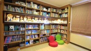 Una biblioteca con múltiples estanterías de madera repletas de libros y diversos objetos decorativos. Dos sillas coloridas se encuentran en primer plano.