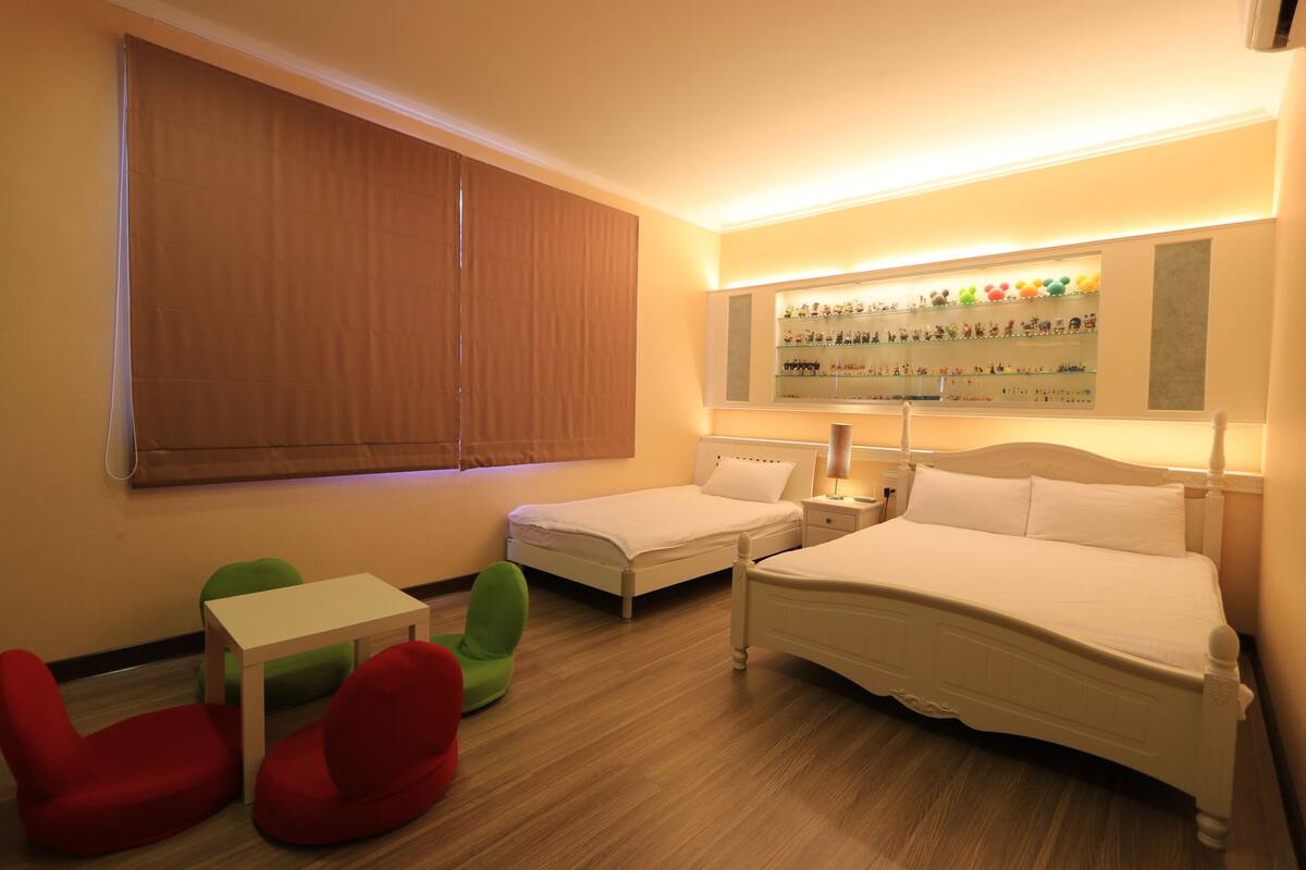 Une chambre d’hôtel avec deux lits, une petite table, une chaise verte et une chaise rouge.