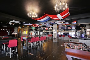 En bardisk med barstolar, ett fotbollsspel och flaggor som hänger från taket.