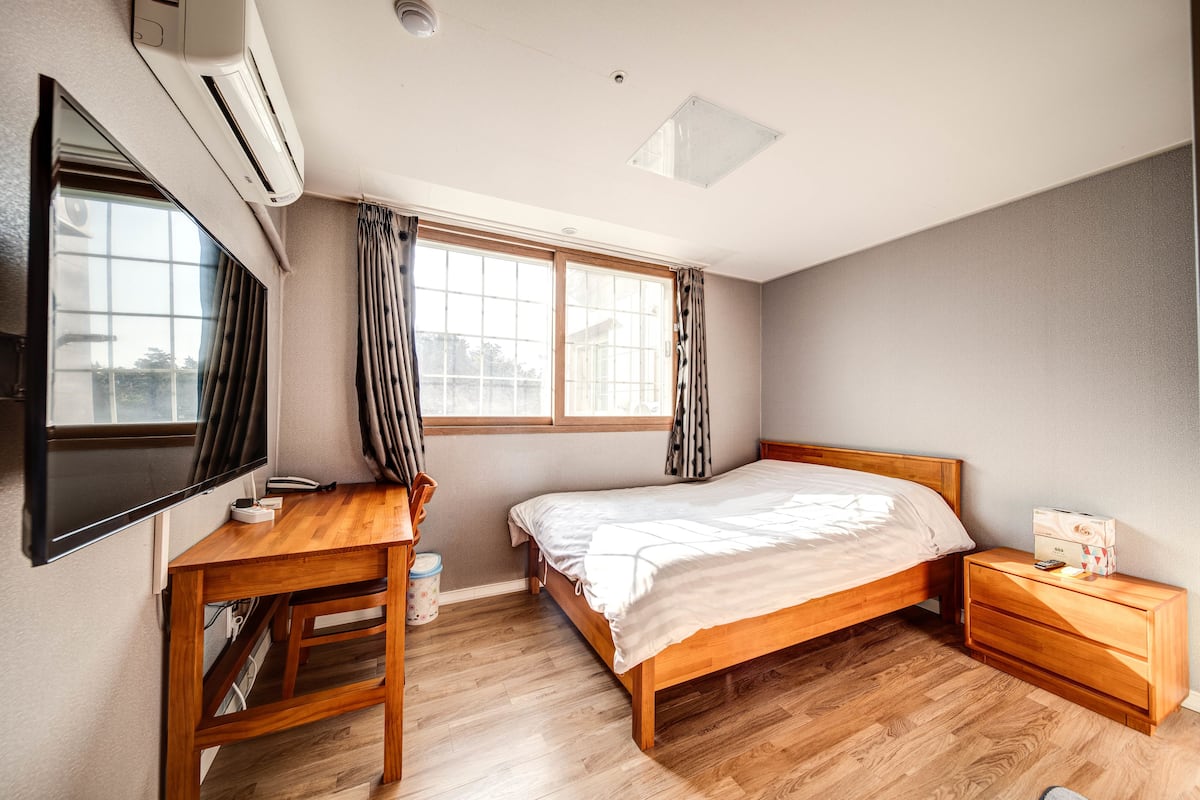 A bedroom with a wooden bed, a desk, and a TV.